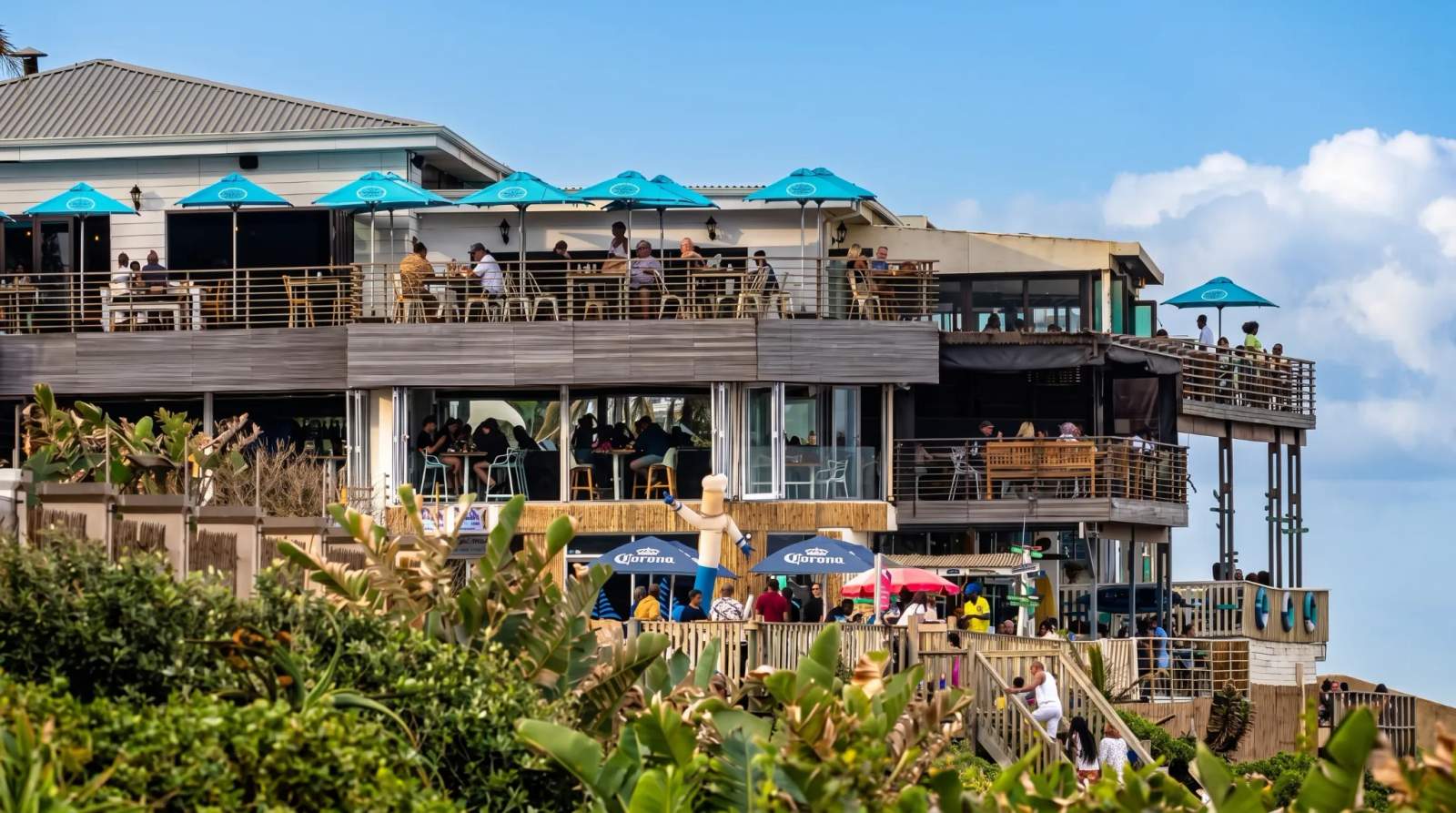 Multilevel beachside restaurant with people dining on balconies, overlooking green foliage in Ballito.