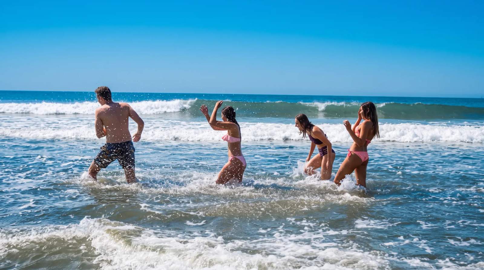 Four friends splashing and playing in the shallow ocean waters at Blythedale beach on a sunny day.