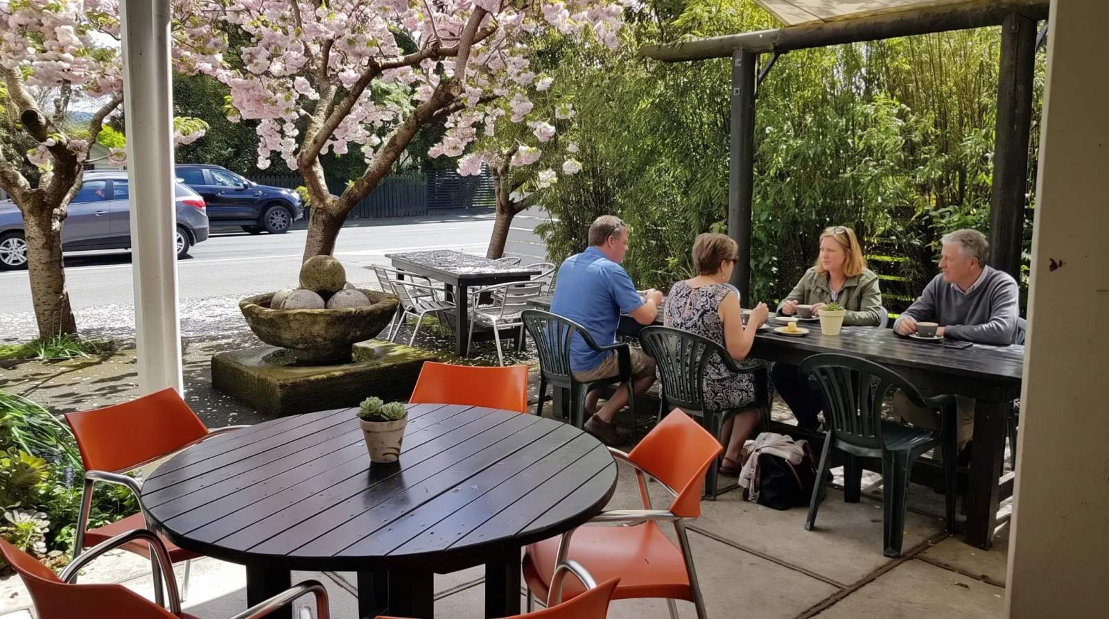 People enjoy coffee and food at an outdoor cafe in Greytown, with pink blossoms overhead.