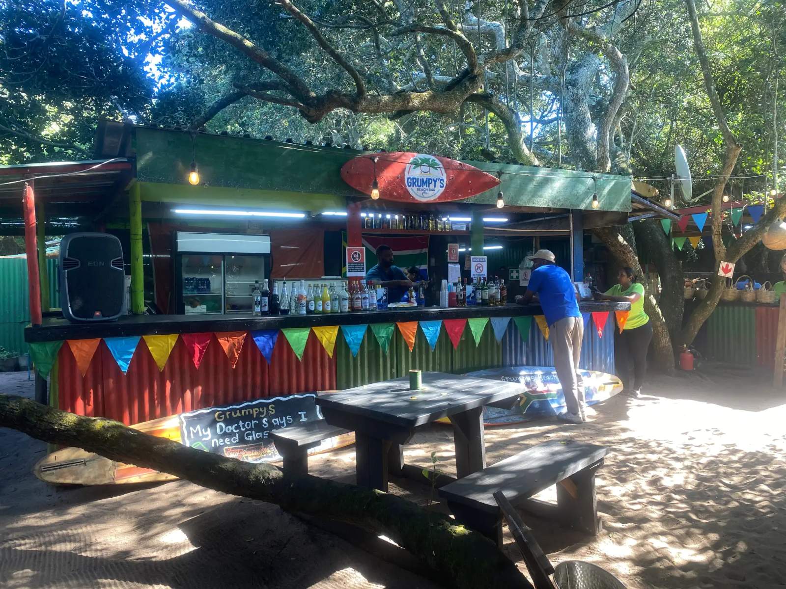 A vibrant casual bar and restaurant on the sandy beach under lush trees in Blythedale.